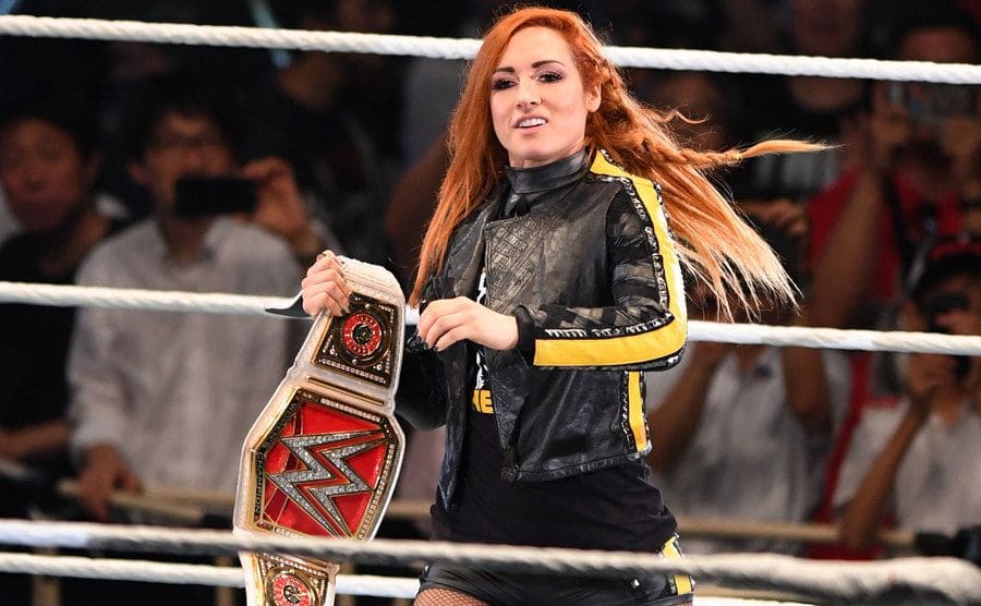 Becky Lynch is entering the ring dressed in a black leather outfit holding the champion belt during the WWE Live Tokyo.