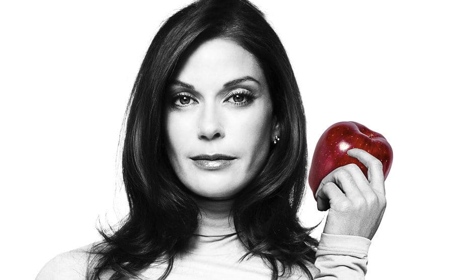 A black and white Teri Hatcher is holding a red apple in the season 1 promo shot.