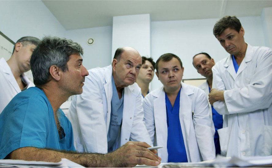 Paolo sits as he explains things to the other doctors in the room. 