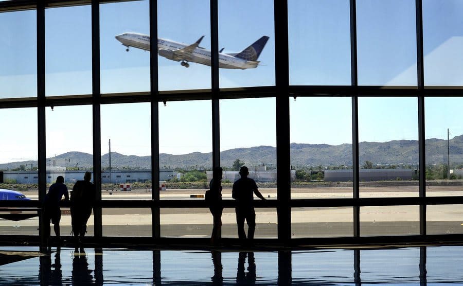 Airline passengers are watching from the terminal as an airplane takes off.