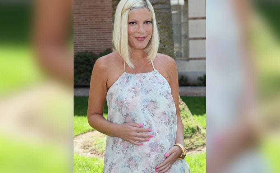 A pregnant Tori Spelling poses outdoors. 