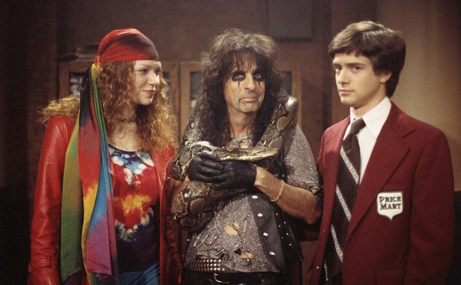 Topher Grace next to Alice Cooper and Laura Prepon in a still from the show. 