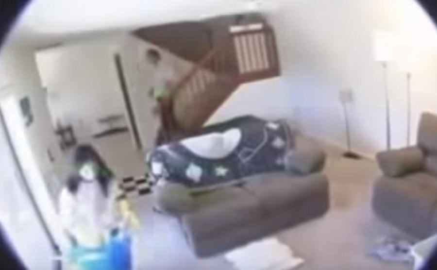 A man and a woman walk around their home as seen through a CCTV camera. 