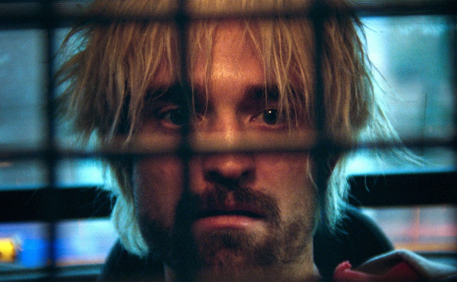 Robert Pattinson stares blankly from the backseat of a cop car. 