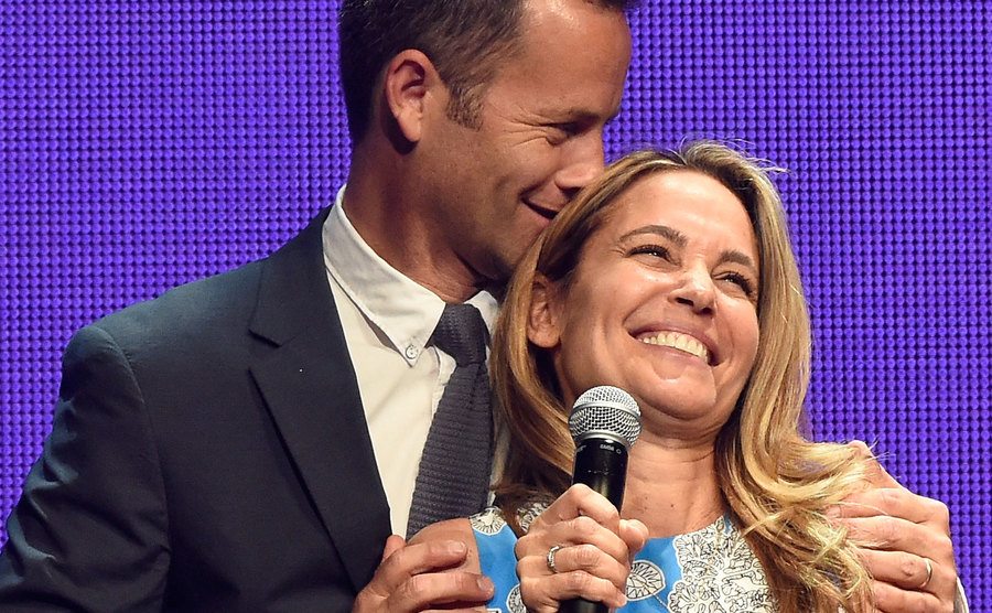 Kirk Cameron embraces his wife as she speaks on stage.