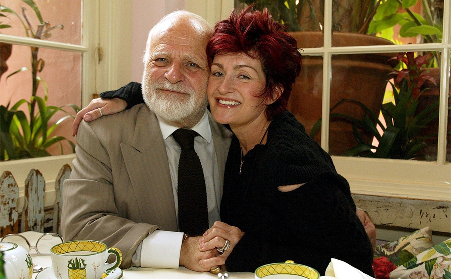 Don Arden e Sharon Osbourne posando juntos em uma mesa de café da manhã 