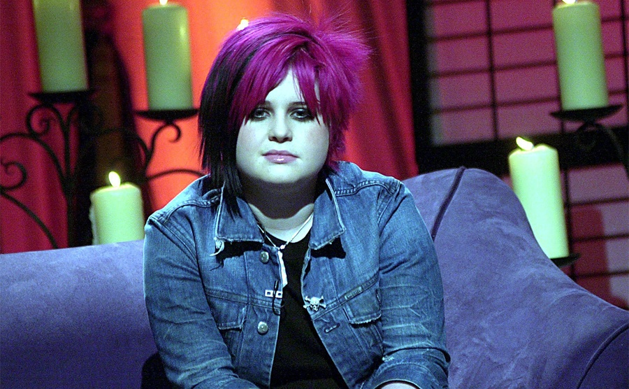 Kelly Osbourne posiert mit pinker Kurzhaarfrisur auf einer Couch 