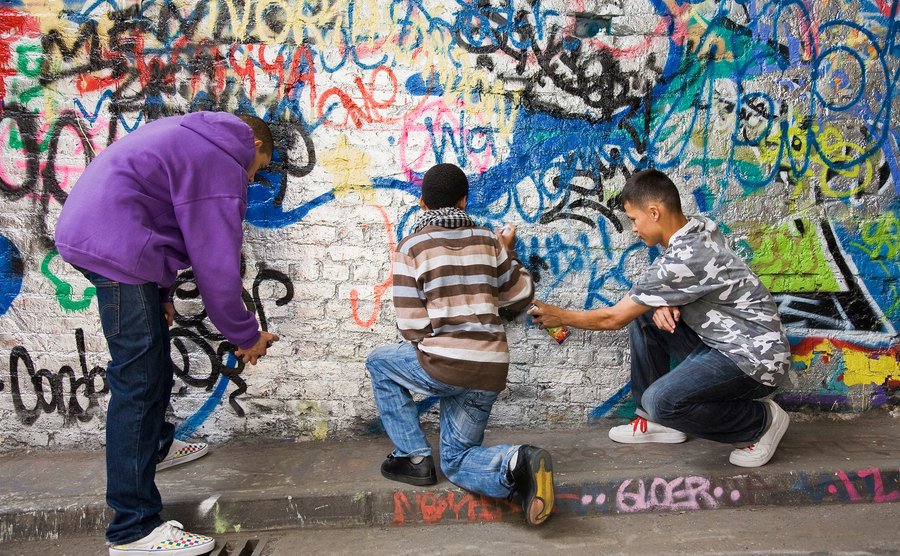Adolescentes pintando grafites em uma parede.