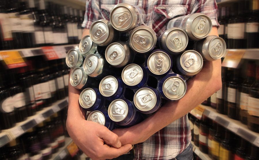 Um jovem carregando muitas latas de cerveja no supermercado.