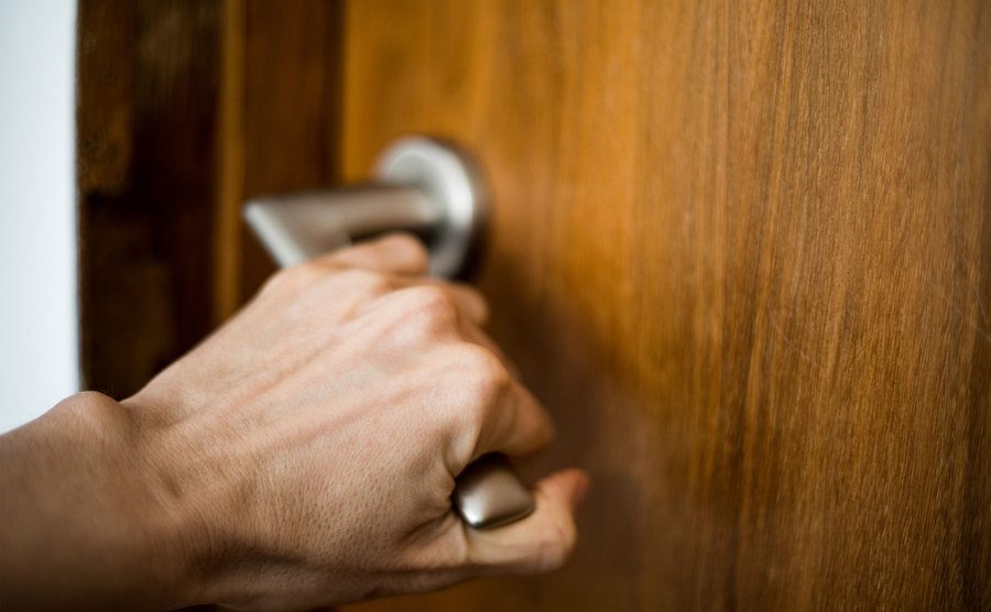 Uma mão tentando abrir a maçaneta de uma porta.