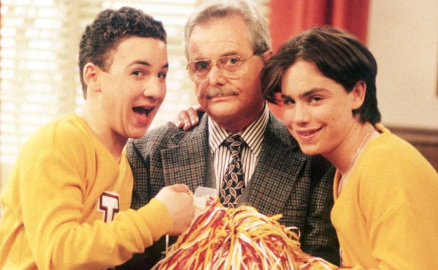 Cory and Shawn embrace Mr. Feeny while they are dressed as cheerleaders. 