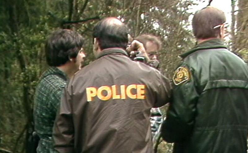 A dated photo of police officers searching a forest for evidence.