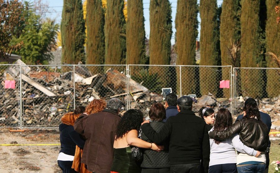 Mourners stand outside the burnt remains of the Ortega family home. 