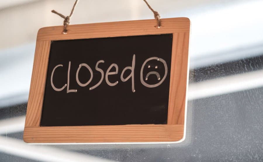 An image of a wooden framed door signage written with chalk “CLOSED.”