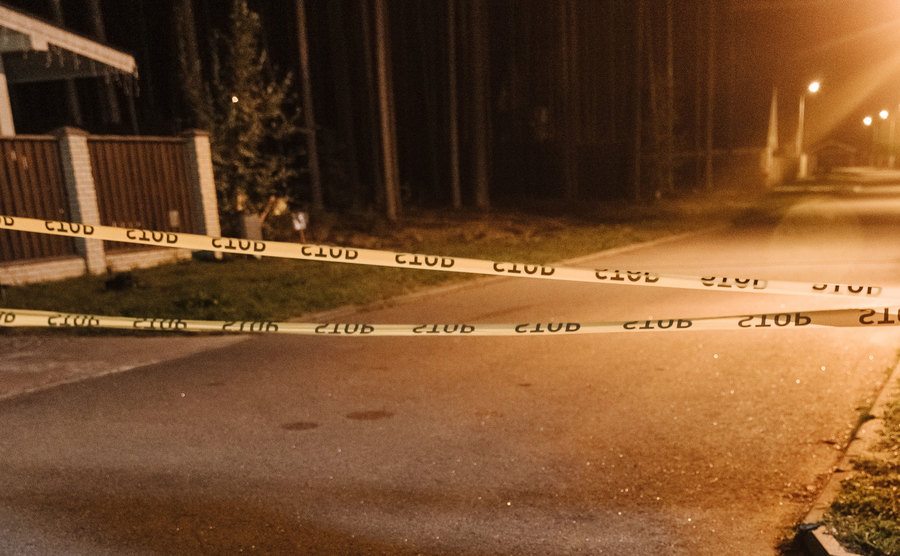 A police tape surrounds a crime scene in a quiet neighborhood at night.