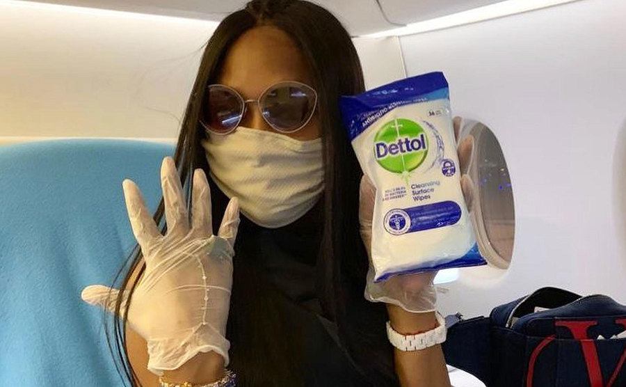 Naomi Campbell sits in a plane fully gloved, masked and ready to clean her seat. 