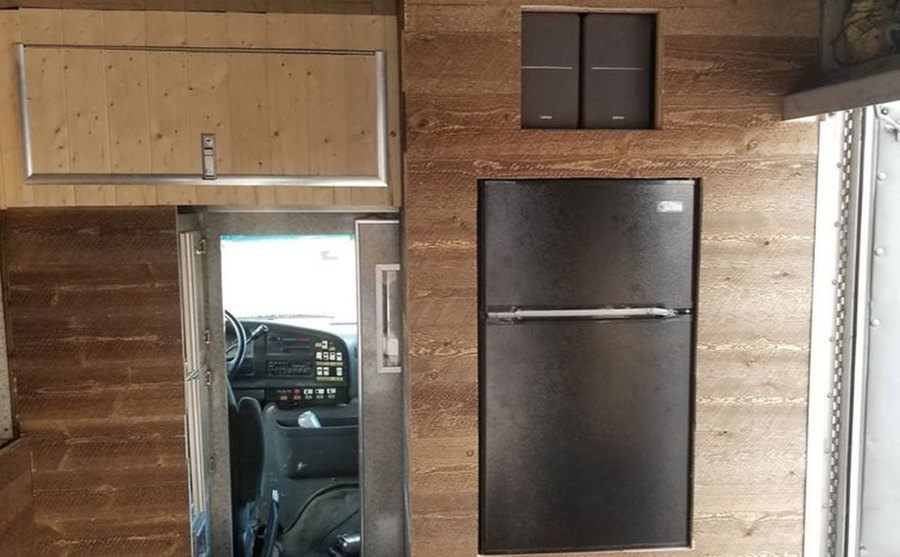 An interior shot of the new fridge and wooden cabinets in the bus. 