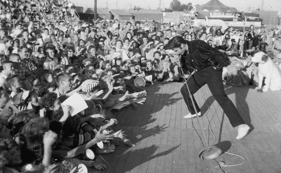 A photo of Elvis Presley performing outdoors on a small stage.