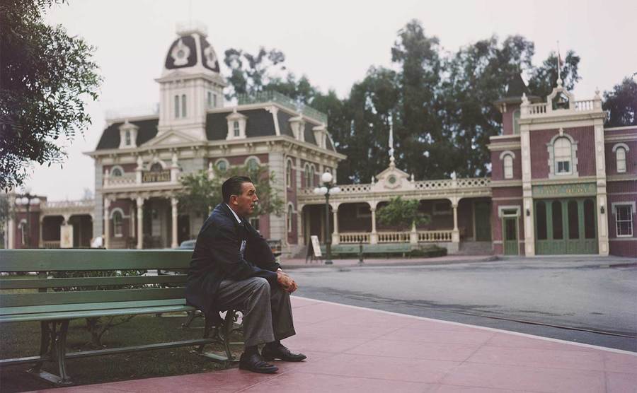 Walt Disney sits on a bench in his Disneyland amusement park. 