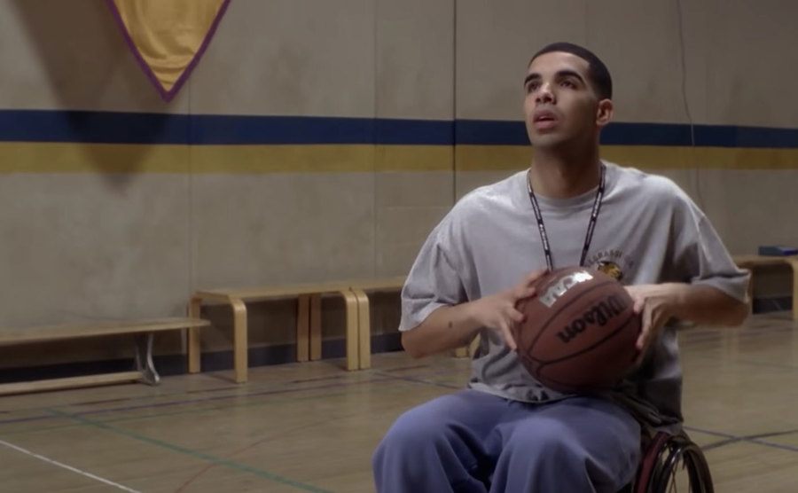 Drake is playing basketball in a wheelchair in a still from Degrassi. 